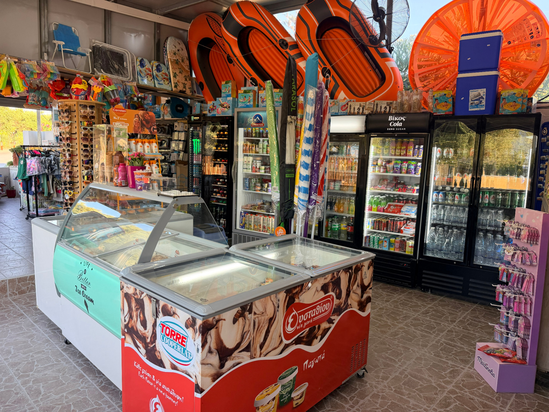 AMOS SEASIDE Mini Market overview with drinks fridges ice cream floaties and sunglasses near JW Marriott Crete
